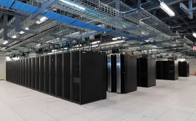 A high-tech data center featuring rows of sleek black server racks under overhead cable trays and bright lighting.