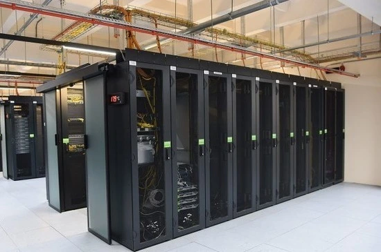 A row of black server racks filled with networking equipment in a data center, illuminated under overhead lights.