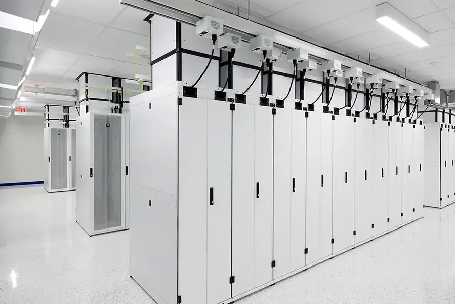 A modern data center with rows of white server cabinets and overhead cables, featuring bright lighting and a clean floor.