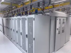 Rows of gray server racks with visible cables and monitoring equipment in a clean, well-lit data center environment.