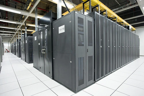 A row of server racks in a data center, showcasing sleek black cabinets and white tile flooring under bright overhead lights.