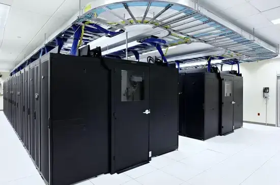 A modern data center with rows of black server cabinets, overhead cable management, and a clean, bright white tiled floor.