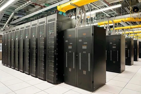 A data center with rows of black server racks, featuring overhead cabling and a spacious tiled floor, showcasing IT infrastructure.